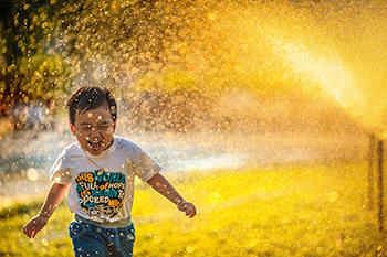 Child running through water spray in hot weather