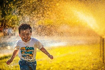 Child running through water spray in hot weather