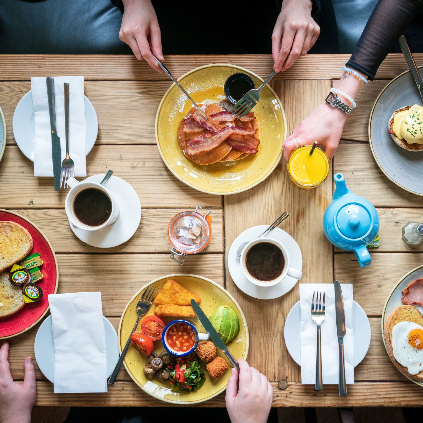 The image shows a table from above laid out with food including, black coffees and pancakes with bacon.