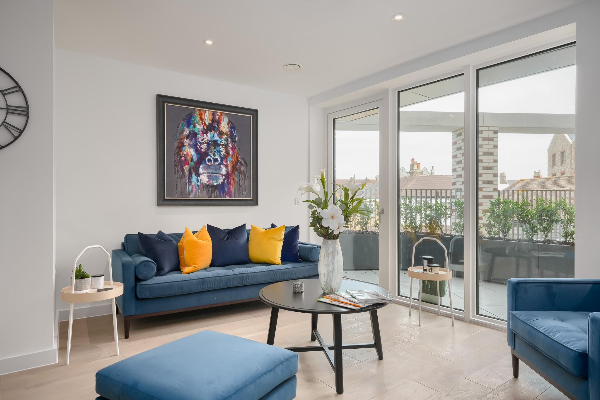 A picture of a showroom apartment which features floor to ceiling windows, a blue sofa and granite coffee table.